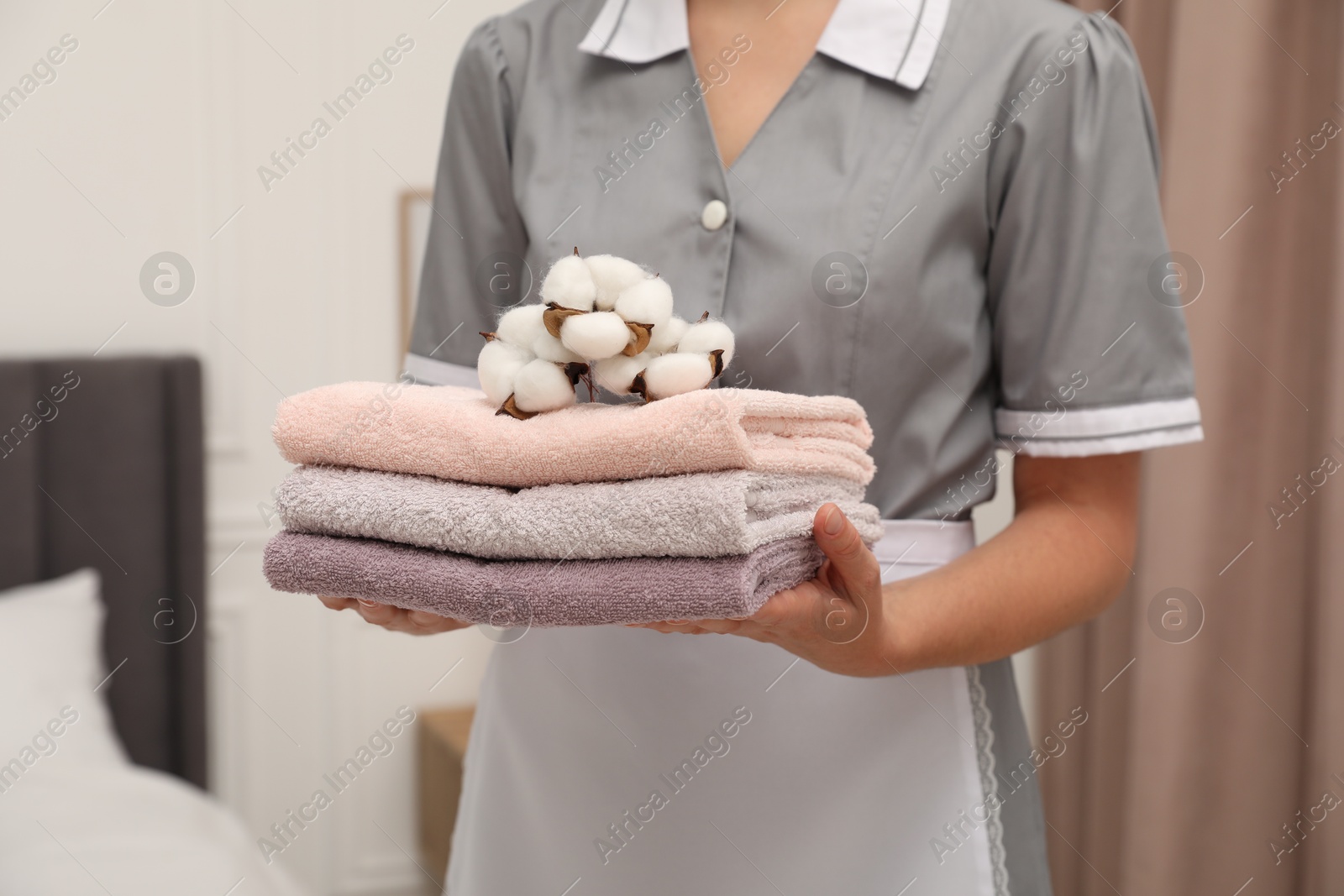 Photo of Chambermaid with stack of terry towels and cotton flowers in hotel room, closeup