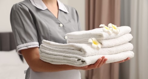 Photo of Chambermaid with stack of white terry towels and plumeria flowers in hotel room, closeup