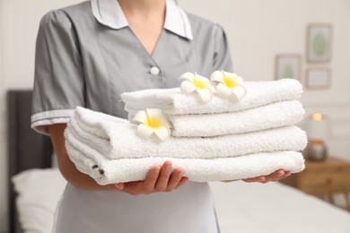 Photo of Chambermaid with stack of white terry towels and plumeria flowers in hotel room, closeup