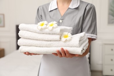 Photo of Chambermaid with stack of white terry towels and plumeria flowers in hotel room, closeup