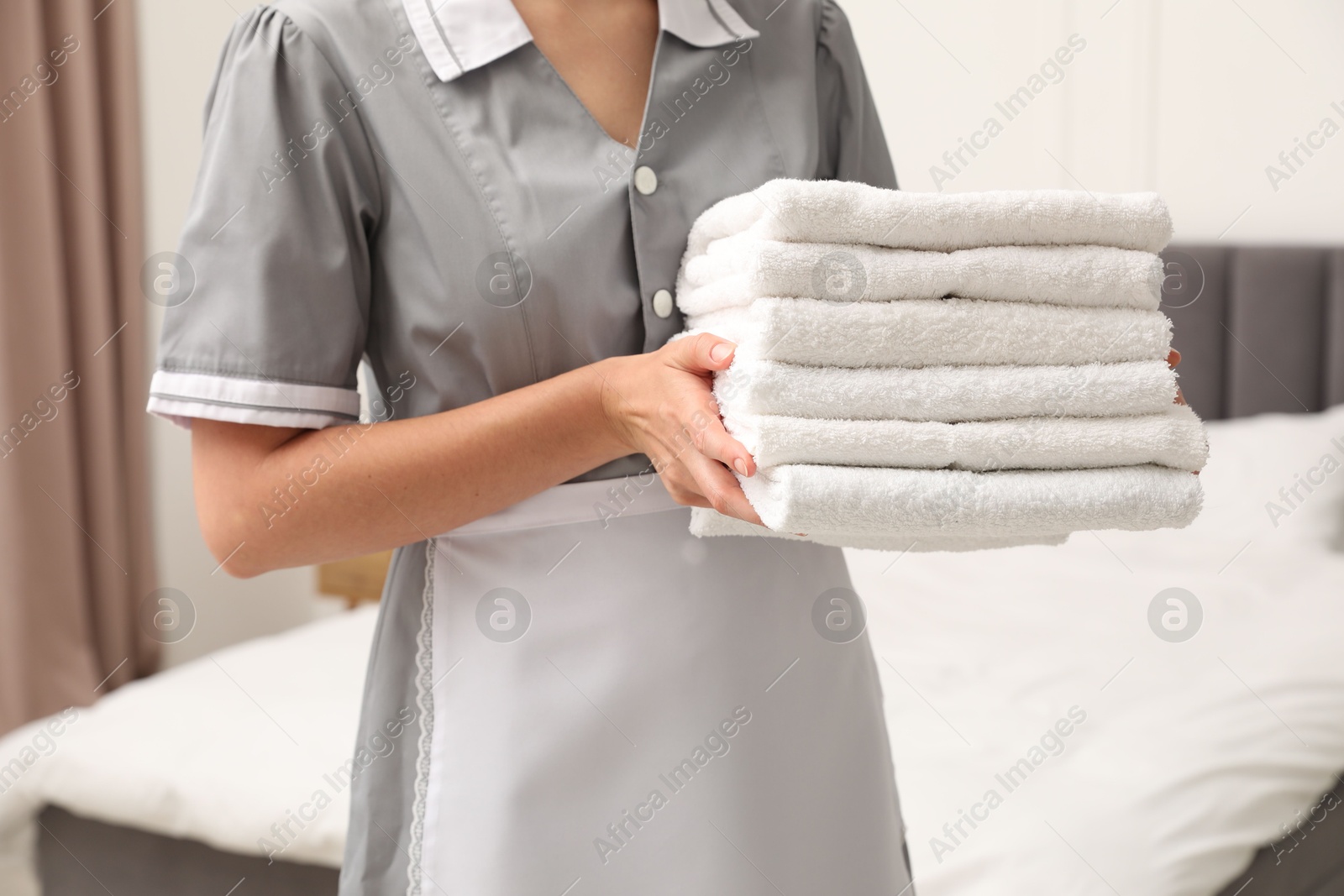 Photo of Chambermaid with stack of white terry towels in hotel room, closeup