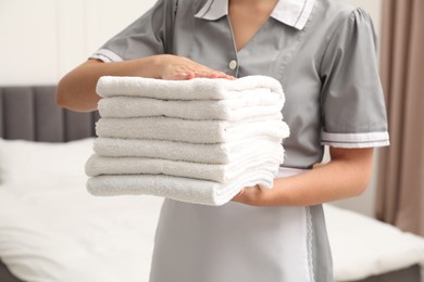 Photo of Chambermaid with stack of white terry towels in hotel room, closeup