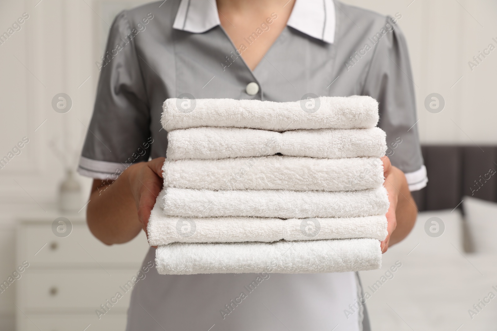 Photo of Chambermaid with stack of white terry towels in hotel room, closeup