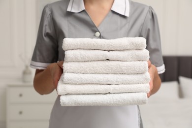 Photo of Chambermaid with stack of white terry towels in hotel room, closeup