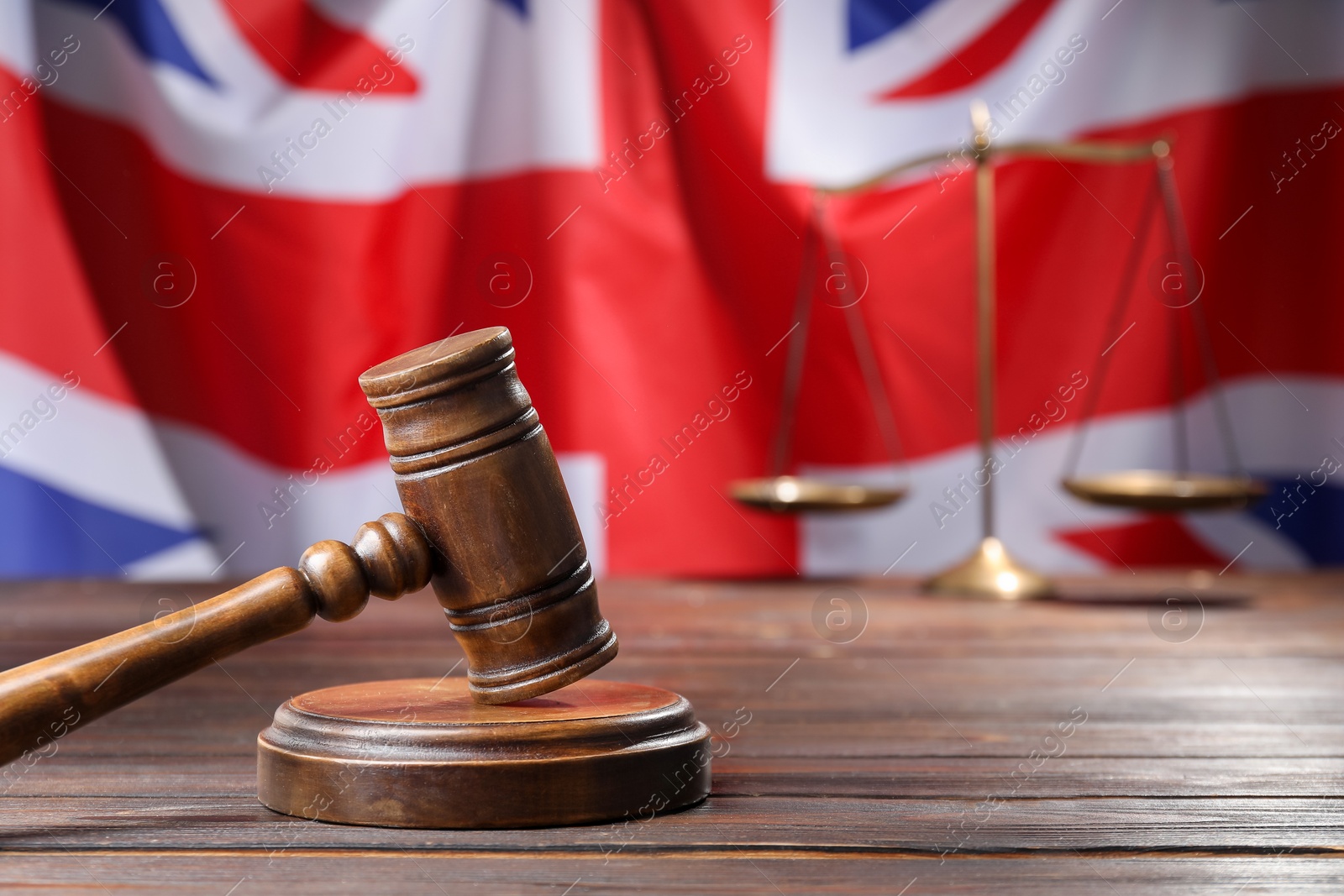Photo of Judge's gavel and scales on wooden table against flag of United Kingdom, closeup. Space for text