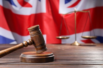 Photo of Judge's gavel and scales on wooden table against flag of United Kingdom, closeup. Space for text