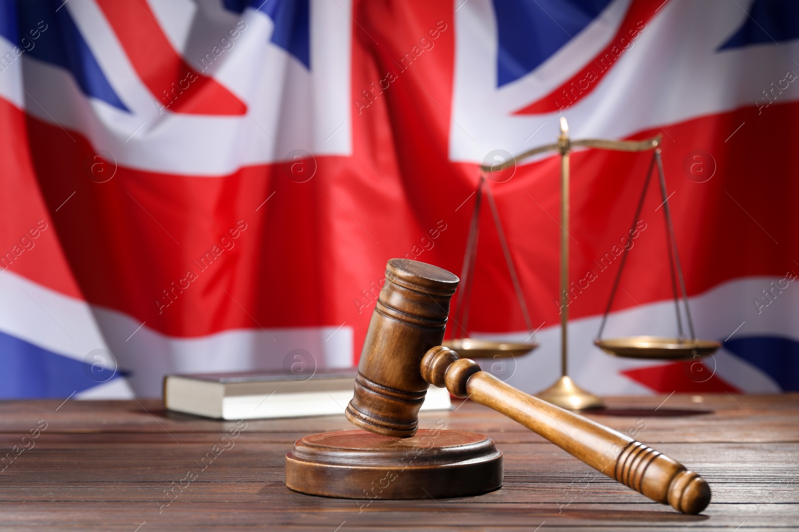 Photo of Judge's gavel, book and scales on wooden table against flag of United Kingdom, closeup