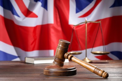Photo of Judge's gavel, book and scales on wooden table against flag of United Kingdom, closeup