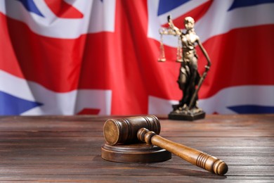 Photo of Judge's gavel and statue of Lady Justice on wooden table against flag of United Kingdom, closeup