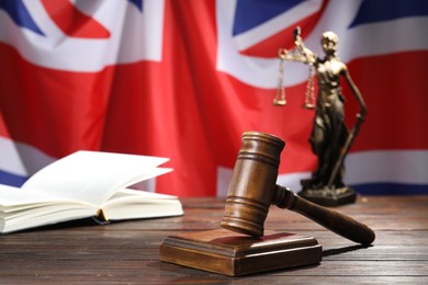 Photo of Judge's gavel, book and statue of Lady Justice on wooden table against flag of United Kingdom, closeup