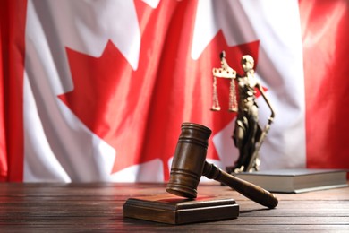 Photo of Judge's gavel, book and statue of Lady Justice on wooden table against flag of Canada, closeup