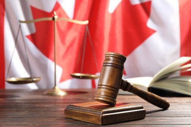 Photo of Judge's gavel, book and scales on wooden table against flag of Canada, closeup