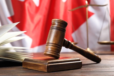 Photo of Judge's gavel, book and scales on wooden table against flag of Canada, closeup