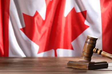 Photo of Judge's gavel on wooden table against flag of Canada, closeup. Space for text
