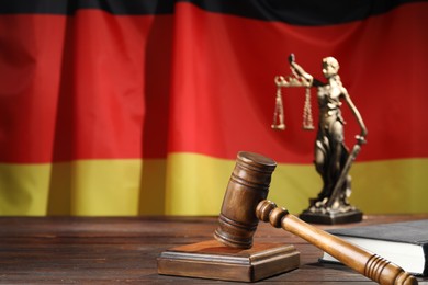 Photo of Judge's gavel, book and statue of Lady Justice on wooden table against flag of Germany, closeup. Space for text