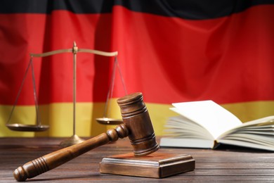 Photo of Judge's gavel, book and scales on wooden table against flag of Germany, closeup