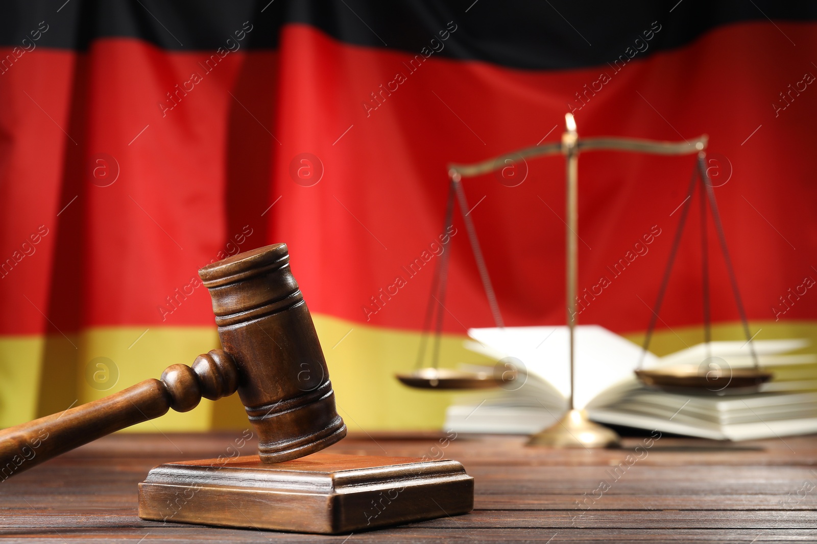 Photo of Judge's gavel, book and scales on wooden table against flag of Germany, closeup