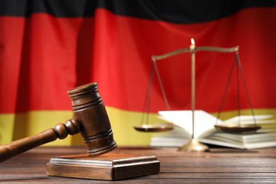 Photo of Judge's gavel, book and scales on wooden table against flag of Germany, closeup