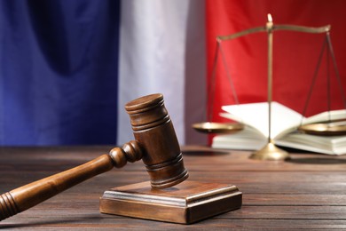 Photo of Judge's gavel, book and scales on wooden table against flag of France, closeup