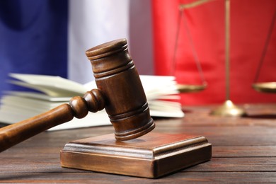 Photo of Judge's gavel, book and scales on wooden table against flag of France, closeup