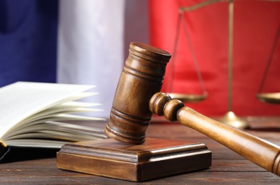 Photo of Judge's gavel, book and scales on wooden table against flag of France, closeup