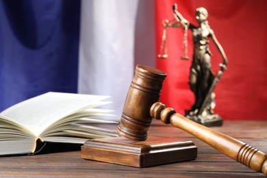 Photo of Judge's gavel, book and statue of Lady Justice on wooden table against flag of France, closeup