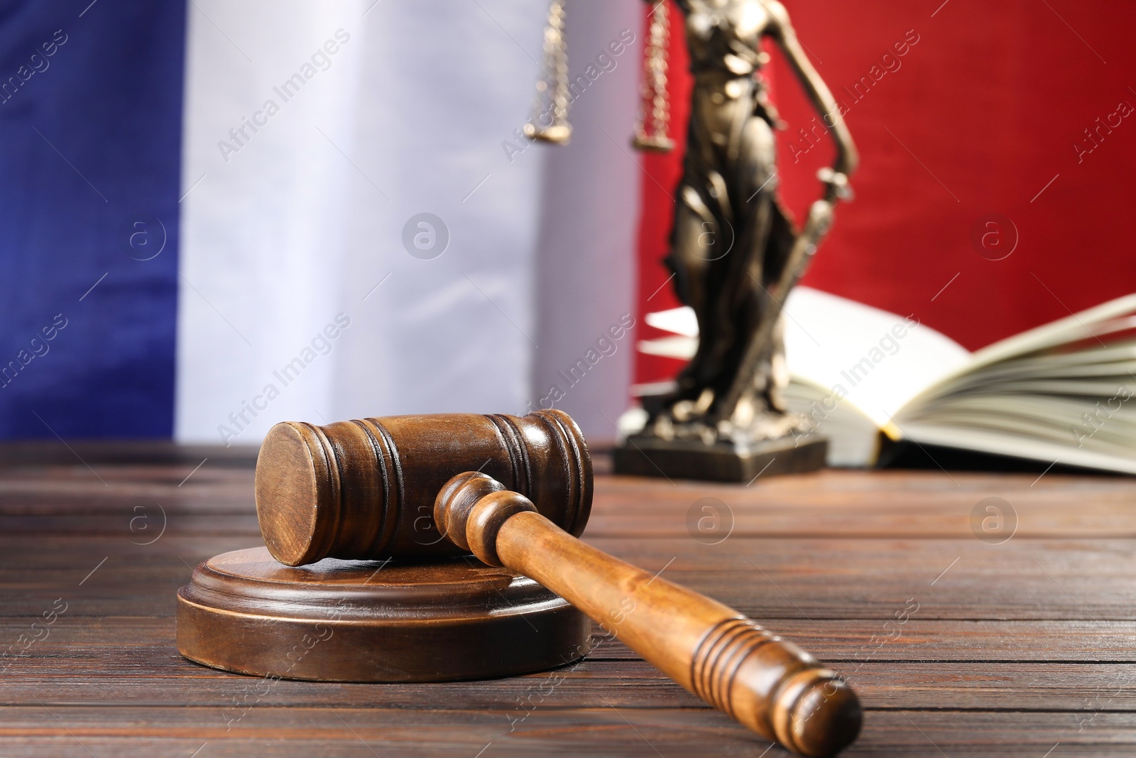 Photo of Judge's gavel, book and statue of Lady Justice on wooden table against flag of France, closeup
