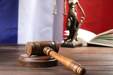 Photo of Judge's gavel, book and statue of Lady Justice on wooden table against flag of France, closeup