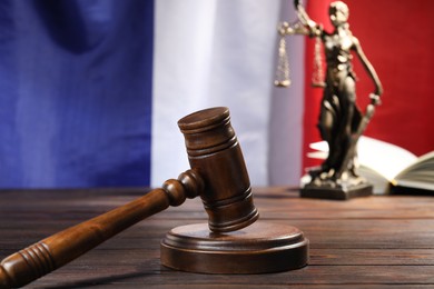 Photo of Judge's gavel, book and statue of Lady Justice on wooden table against flag of France, closeup