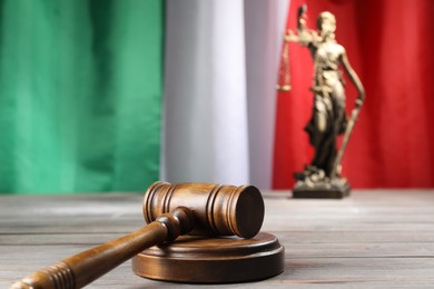 Photo of Judge's gavel and statue of Lady Justice on wooden table against flag of Italy, closeup