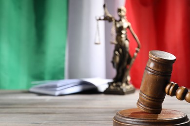 Photo of Judge's gavel, book and statue of Lady Justice on wooden table against flag of Italy, closeup. Space for text