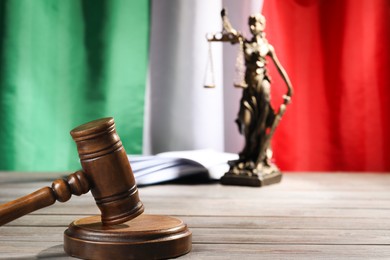Photo of Judge's gavel, book and statue of Lady Justice on wooden table against flag of Italy, closeup. Space for text