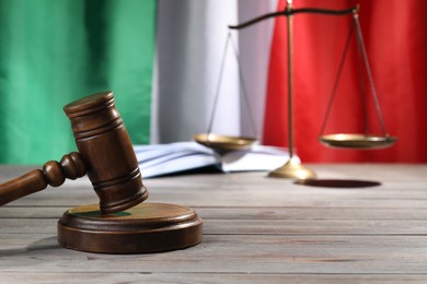 Photo of Judge's gavel, book and scales on wooden table against flag of Italy, closeup. Space for text