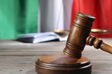 Photo of Judge's gavel, book and scales on wooden table against flag of Italy, closeup. Space for text
