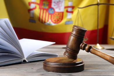 Photo of Judge's gavel, book and scales on wooden table against flag of Spain, closeup