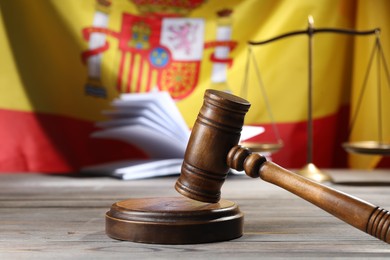 Photo of Judge's gavel, book and scales on wooden table against flag of Spain, closeup