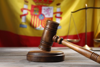 Photo of Judge's gavel and scales on wooden table against flag of Spain, closeup