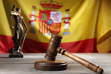 Photo of Judge's gavel and statue of Lady Justice on wooden table against flag of Spain, closeup
