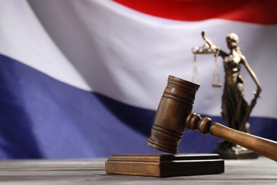 Photo of Judge's gavel and statue of Lady Justice on wooden table against flag of Netherlands, closeup. Space for text