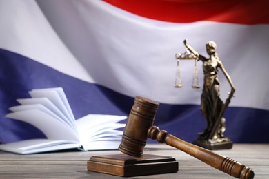 Photo of Judge's gavel, book and statue of Lady Justice on wooden table against flag of Netherlands, closeup