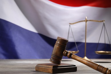 Photo of Judge's gavel and scales on wooden table against flag of Netherlands, closeup. Space for text