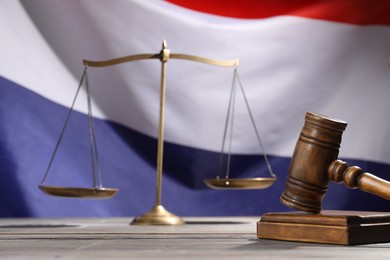 Photo of Judge's gavel and scales on wooden table against flag of Netherlands, closeup