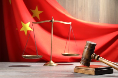 Photo of Judge's gavel and scales on wooden table against flag of China, closeup