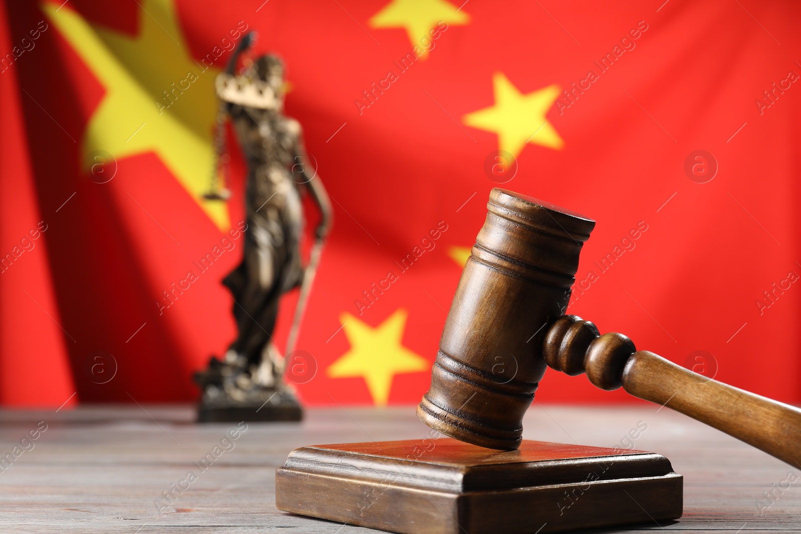 Photo of Judge's gavel and statue of Lady Justice on wooden table against flag of China, closeup. Space for text