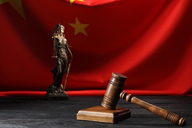 Photo of Judge's gavel and statue of Lady Justice on black wooden table against flag of China, closeup