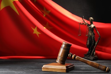 Photo of Judge's gavel and statue of Lady Justice on black wooden table against flag of China, closeup