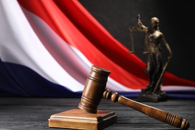 Photo of Judge's gavel, flag of France and statue of Lady Justice on black wooden table, closeup
