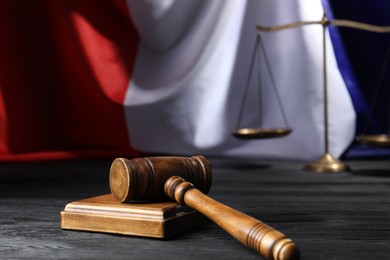 Photo of Judge's gavel and scales on black wooden table against flag of France, closeup