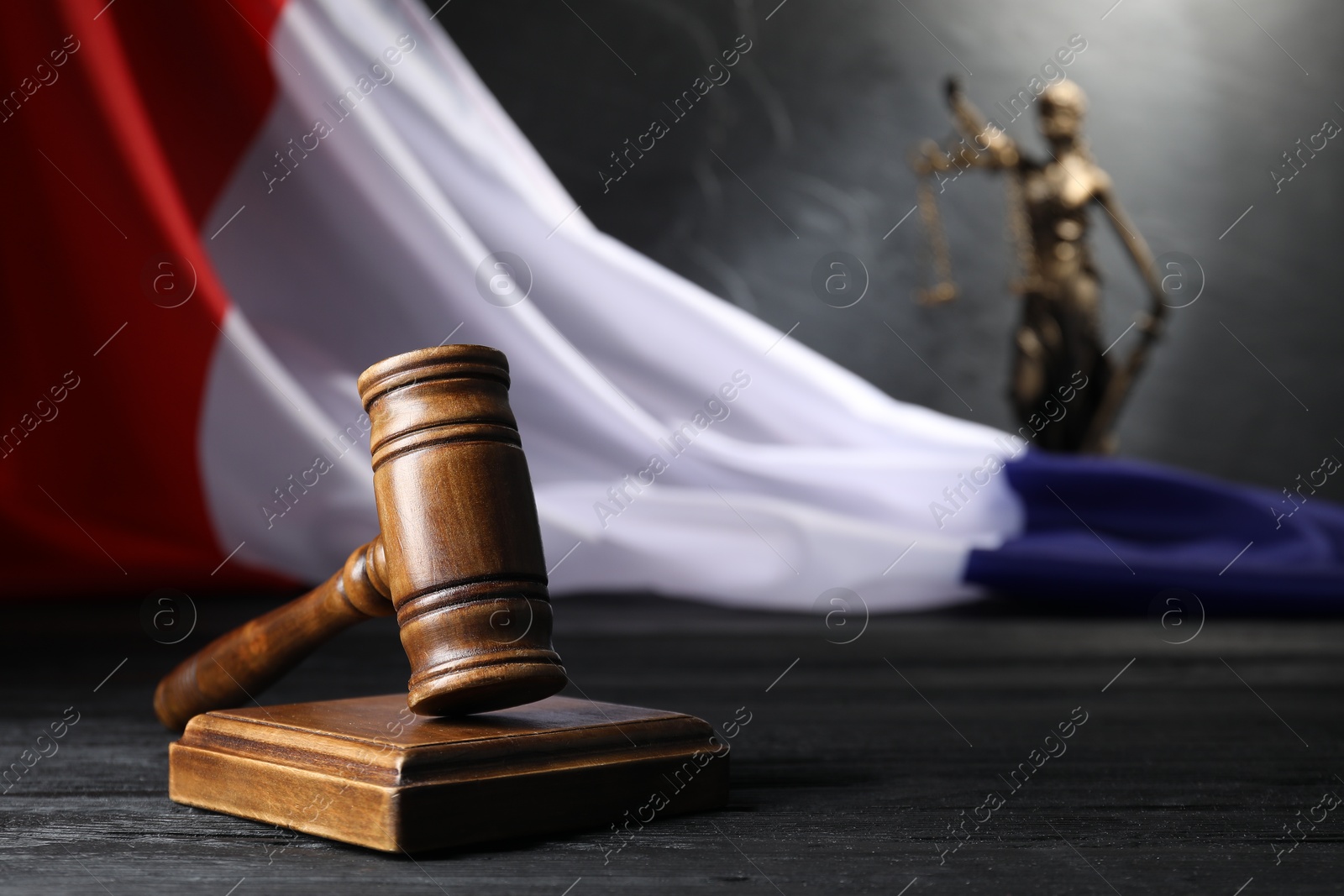 Photo of Judge's gavel, flag of France and statue of Lady Justice on black wooden table, closeup