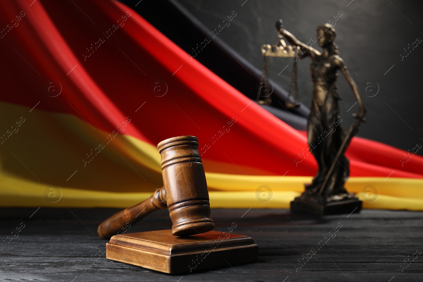 Photo of Judge's gavel, flag of Germany and statue of Lady Justice on black wooden table, closeup